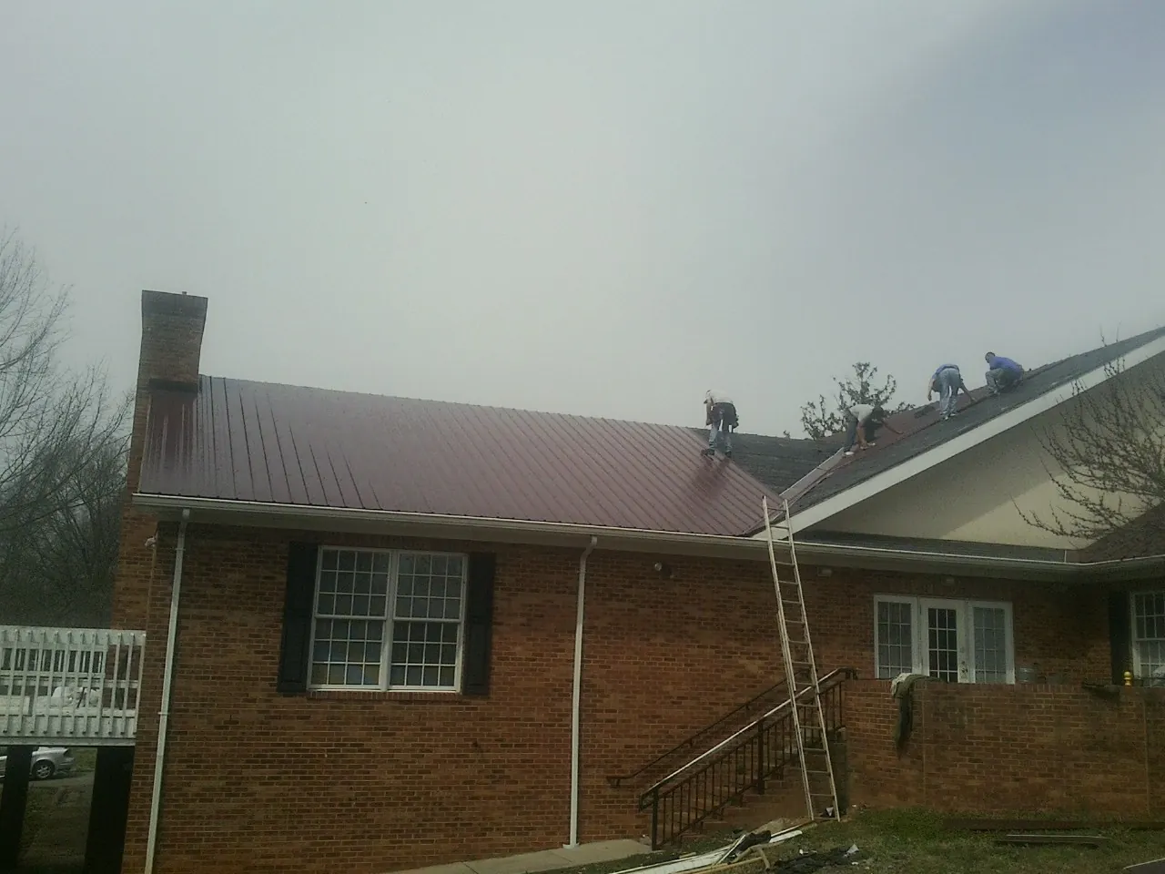 Crew setting red metal roofing panels on a brick home in Etna